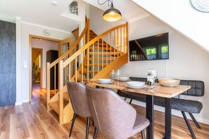 A dining area with a wooden table, two chairs, a black cushioned bench, and a staircase with wooden railings. - Ferienwohnung mit Balkon in St.peter-ording (St. Peter-Ording)