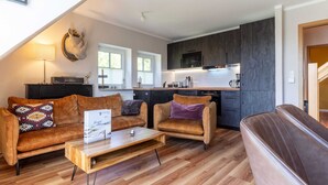 A modern living room with a sofa, armchair, and coffee table, a kitchen with dark cabinets and a microwave, and a large window providing natural light. - Ferienwohnung mit Balkon in St.peter-ording (St. Peter-Ording)