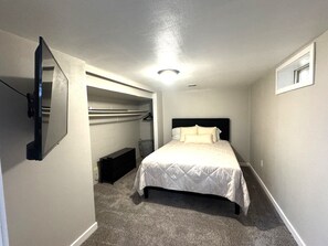 A bedroom with a bed, a built-in closet, a bedside table, and a wall-mounted TV.