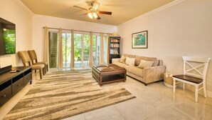 Ein geräumiges Wohnzimmer mit großem Fenster, Deckenventilator, Sofa, Couchtisch und Bücherregal.