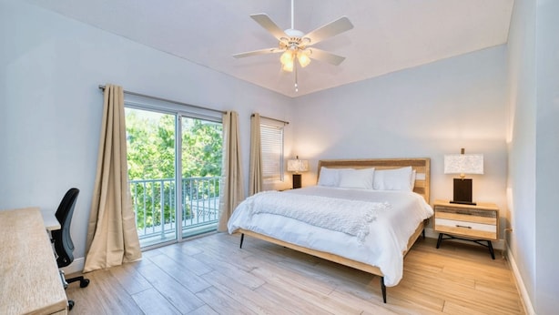 Ein Schlafzimmer mit Bett, Schreibtisch, Stuhl, Deckenventilator und Blick ins Freie durch eine Schiebetür.