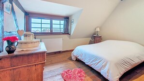 A bedroom with a sloped ceiling, a wooden dresser, a bed with white bedding, a heart-shaped rug, and a window with curtains. - La Perle du Ried n°9 - Alsatian charm between Strasbourg, Colmar and Europapark (Boofzheim)