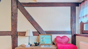 A wooden chest with a lamp, a framed picture, and a heart-shaped pillow in a room with exposed wooden beams. - La Perle du Ried n°8 - Alsatian charm & serenity, just a stone's throw from Europa-Park (Boofzheim)