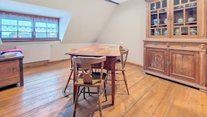 A dining area with a wooden table and chairs, a cabinet with glass doors, and a window with patterned curtains. - La Perle du Ried n°8 - Alsatian charm & serenity, just a stone's throw from Europa-Park (Boofzheim)