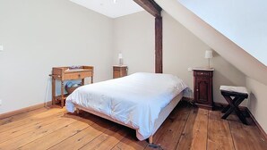 A bedroom with a wooden floor, a bed with white bedding, a wooden nightstand, a small table, and a lamp. - La Perle du Ried n°8 - Alsatian charm & serenity, just a stone's throw from Europa-Park (Boofzheim)