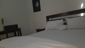 A neatly made bed with white linens, a wooden headboard, and two white pillows. - Origin Ventures Hostel (Moshi)