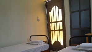 A room with two single beds, a wooden headboard, a small table, and a window with a view of the outside. - Origin Ventures Hostel (Moshi)