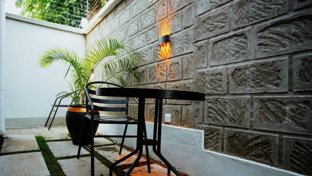 A patio with a black metal table and chair, a potted plant, and a stone wall with a fire feature. - Origin Ventures Hostel (Moshi)
