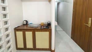Habitación pequeña con escritorio de madera, hervidor de agua, caja de pañuelos y estante bajo.
