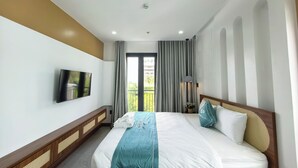 Une chambre d’hôtel avec un lit, un téléviseur fixé au mur, une fenêtre avec des rideaux et un balcon donnant sur des immeubles.