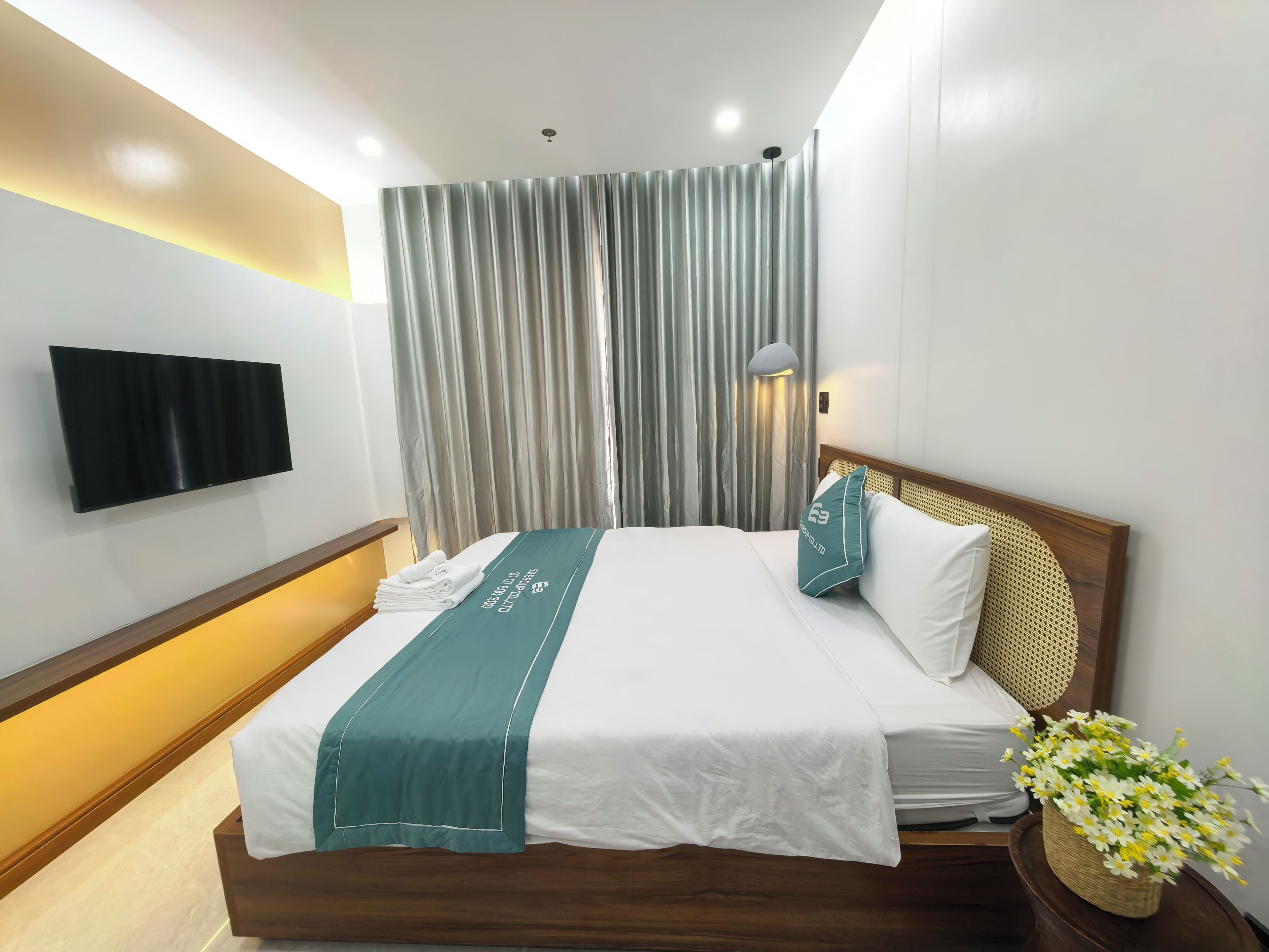 Camera d'albergo con un letto, una TV a schermo piatto, una lampada a parete e un vaso decorativo con fiori.