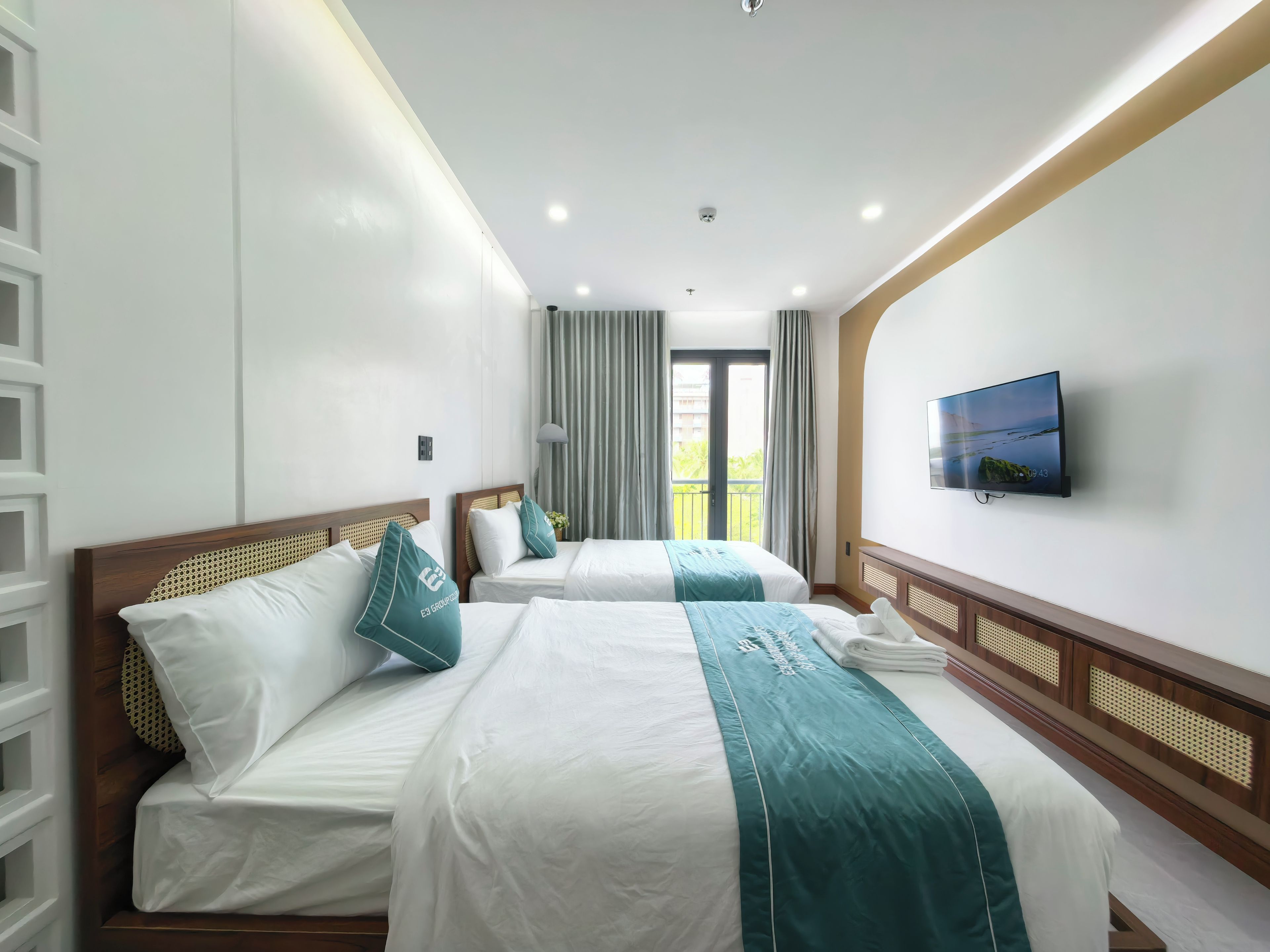 Habitación de hotel con dos camas, televisión y balcón con cortinas.