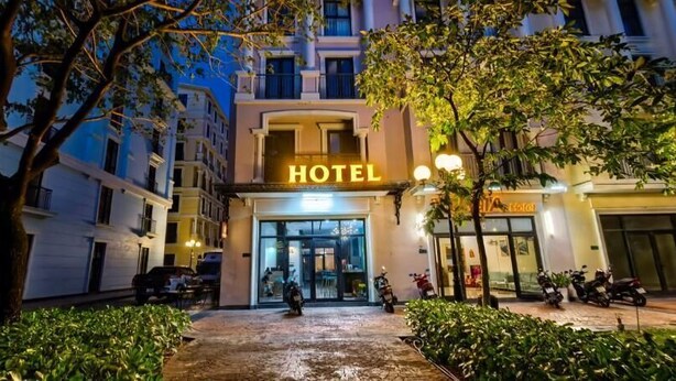 Entrada de hotel con un letrero, un camino pavimentado y follaje circundante.