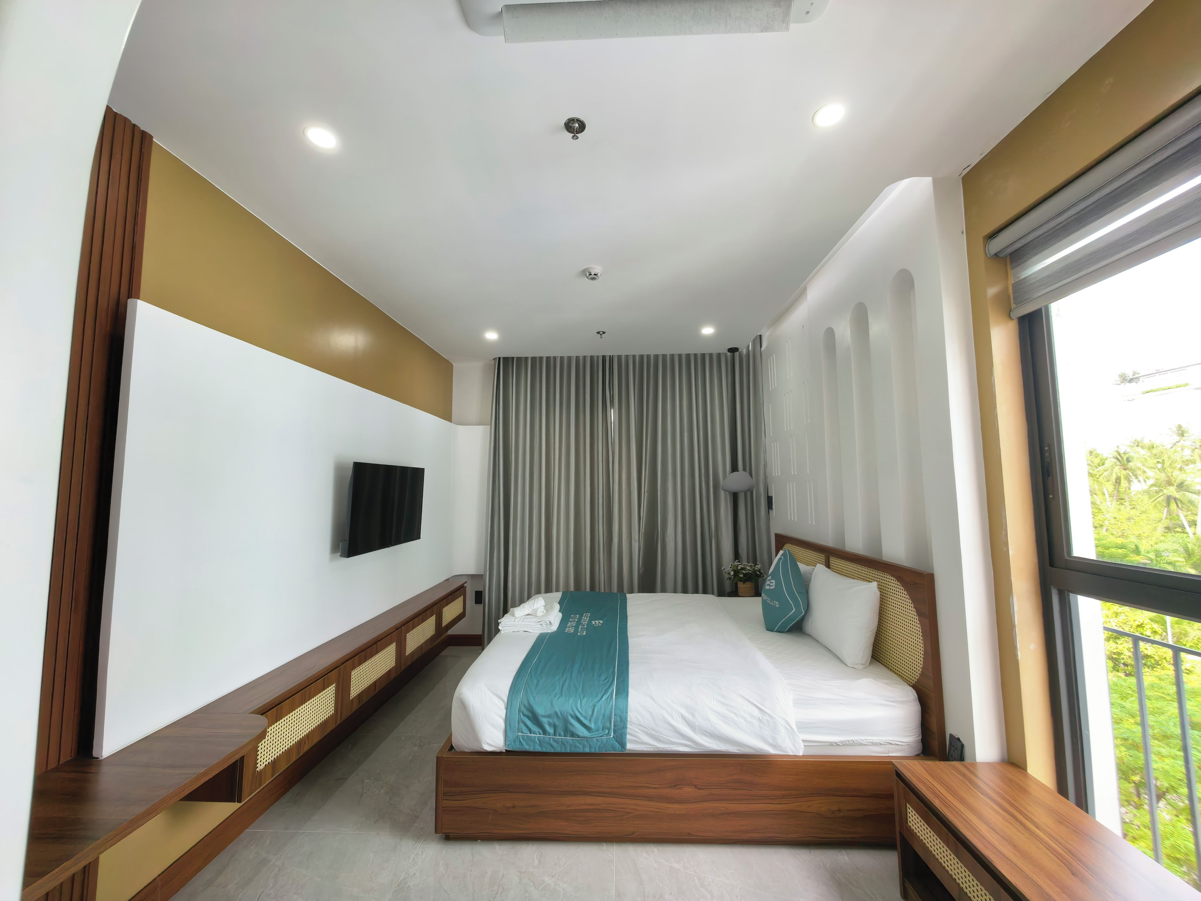Habitación de hotel moderna con una cama grande, un televisor de pantalla plana, una ventana con vistas a zonas verdes e iluminación empotrada en el techo.