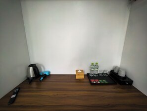 A wooden table with a kettle, a remote control, a blue lighter, two water bottles, a box of tissues, and a tray with tea bags. - Le Boutique Hotel Phu Quoc (Phu Quoc)