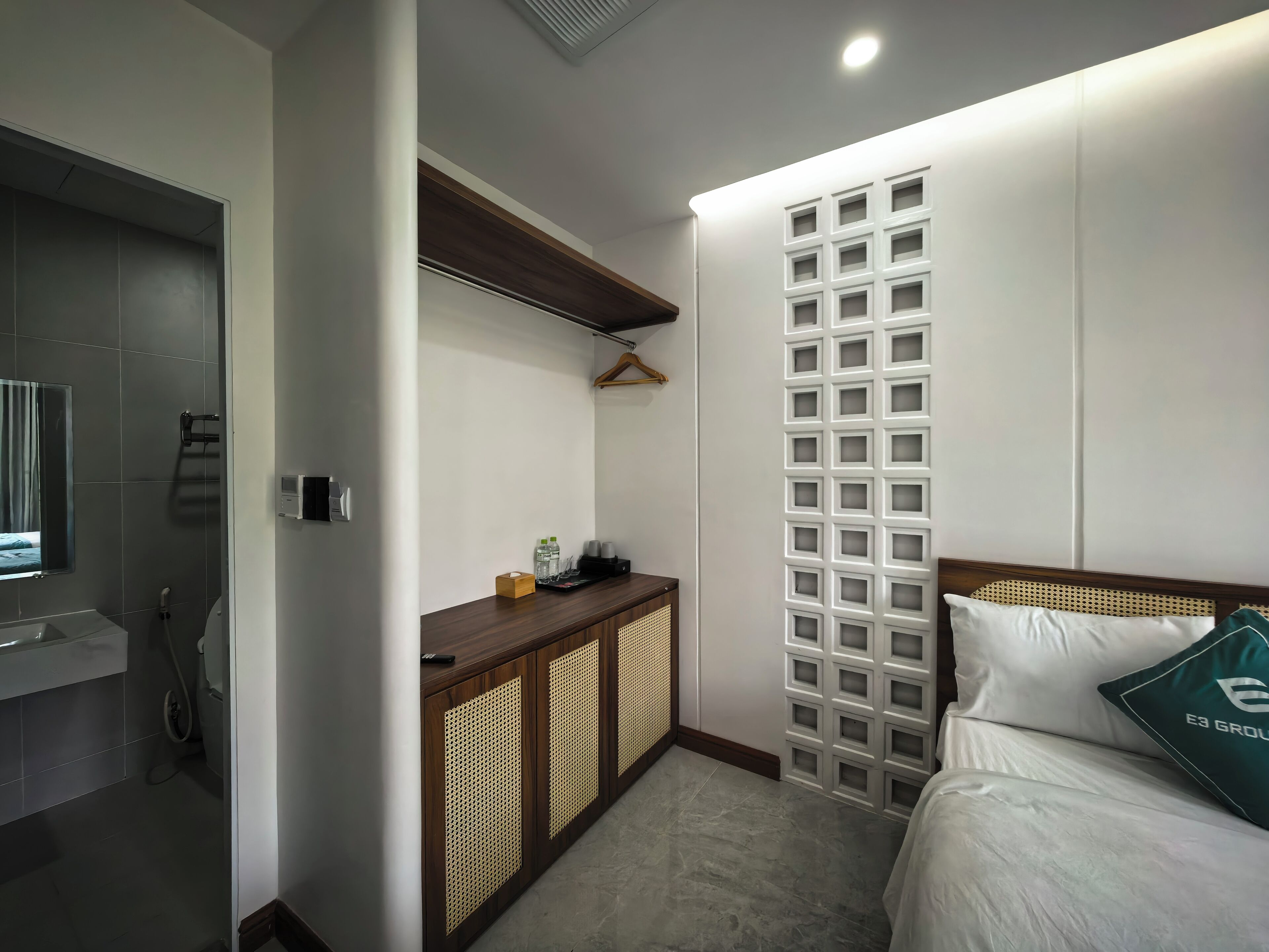 A modern hotel room with a bed, a wooden cabinet, a wall-mounted TV, and a bathroom with a shower and toilet.