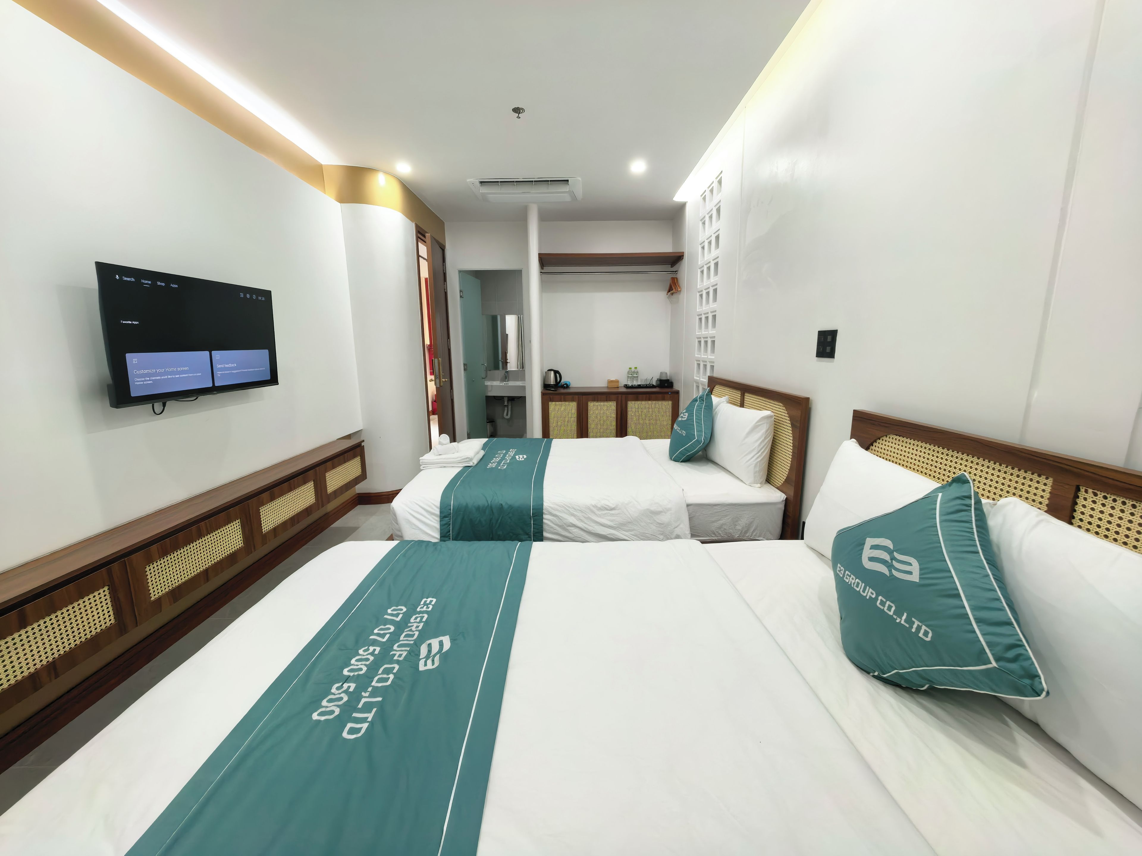 A hotel room with two beds, a TV on the wall, and a bathroom visible through an open door.