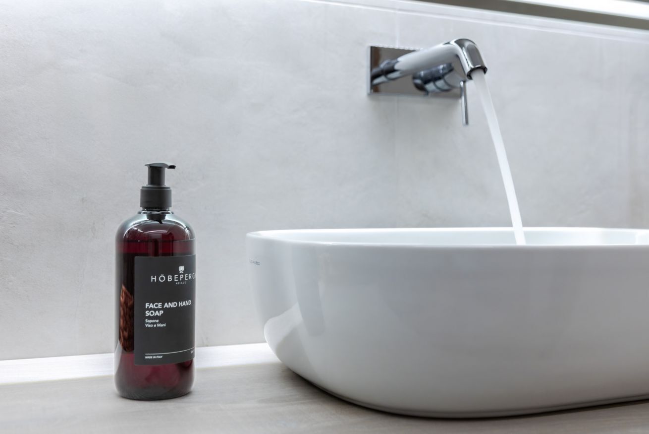 A bathroom with a white basin, a bottle of face and hand soap, and a faucet.
