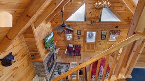 Ein Holzblockbau-Innenraum mit Kamin aus Stein, Deckenventilator und einer Treppe.