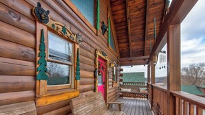 Eine Holzjagdhütte mit Veranda, einer Bank und einem Fenster mit einer Baumdekoration.