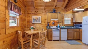 Ein Holzblockhaus-Interieur mit einem Esstisch, Stühlen, einem Herd, einer Mikrowelle und Schränken.