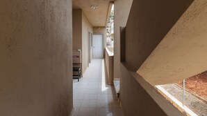 A narrow corridor with a white door at the end, tiled floor, and a balcony with a metal railing. - Sunny Vibes Stalis by Estia (Stalida)