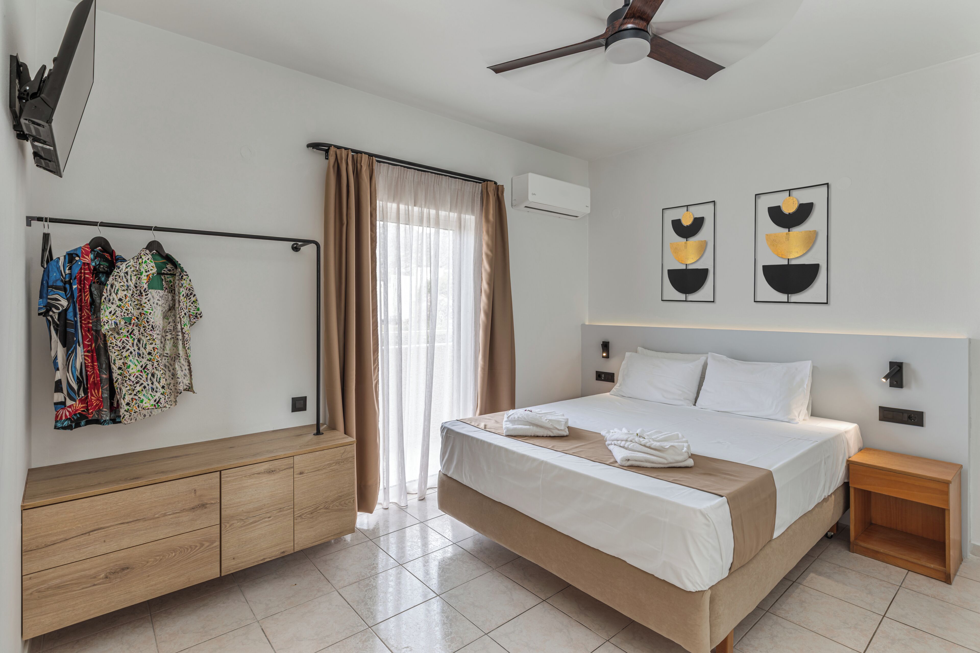 Une chambre d’hôtel avec un lit, une commode en bois, un ventilateur de plafond et une fenêtre avec des rideaux.
