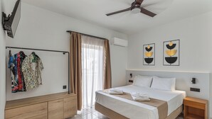 A hotel room with a bed, a wooden dresser, a ceiling fan, and a window with curtains. - Sunny Vibes Stalis by Estia (Stalida)
