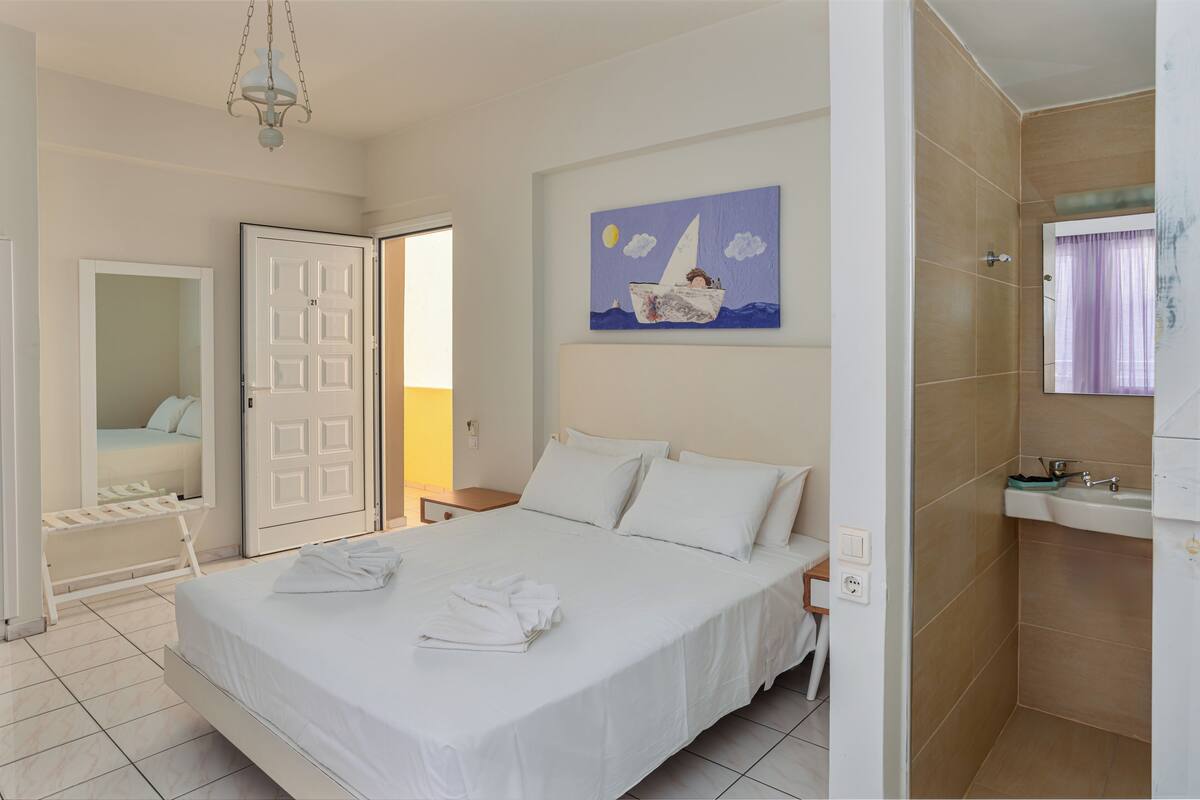 A hotel room with a bed, a painting, a bathroom, and a window with curtains.