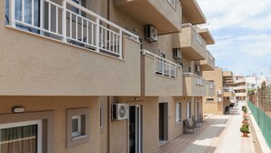 A multi-story residential building with balconies, air conditioning units, and a tiled walkway. - Sunny Vibes Stalis by Estia (Stalida)