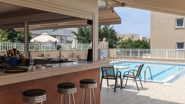 A poolside bar with stools, a pool, and a view of the surrounding area. - Sunny Vibes Stalis by Estia (Stalida)