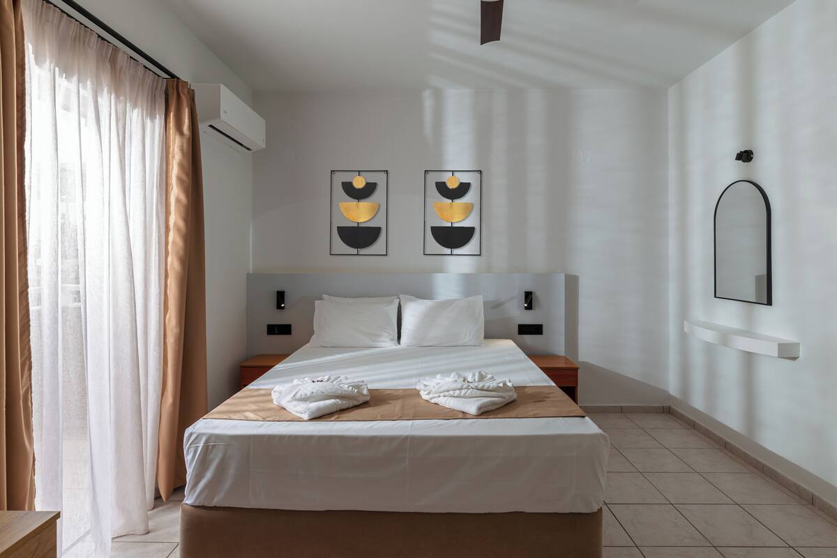 A hotel room with a bed, a nightstand, a wall-mounted mirror, and two wall art pieces.