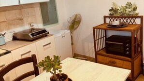 Une cuisine avec des meubles blancs, une table en bois ornée d’une plante en pot, un ventilateur et un four encastré.