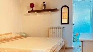Une chambre à coucher avec un lit, un radiateur, une étagère avec une lampe et une porte donnant sur l’extérieur.