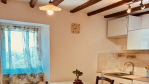 Une cuisine avec une table à manger, des chaises, une plante en pot, une horloge et une fenêtre avec des rideaux.