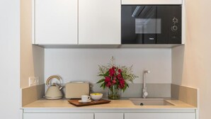 A modern kitchen with white cabinetry, a black microwave, a kettle, a toaster, a sink, and a vase with flowers. - L'Hostalet de Cabrils (Cabrils)