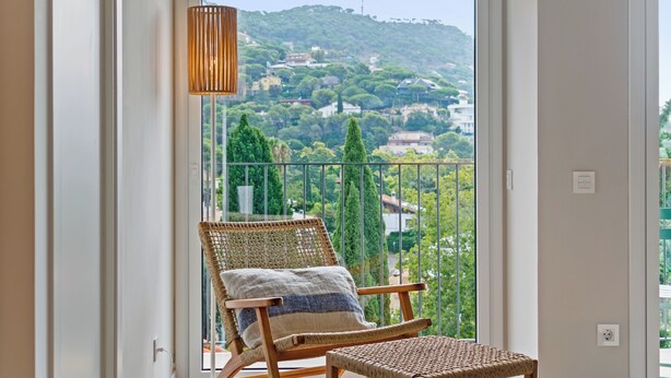 A balcony with a wicker chair and a small table, overlooking a green landscape with trees and buildings. - L'Hostalet de Cabrils (Cabrils)