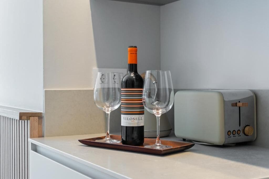 Una encimera de cocina con una botella de vino Vilosell, dos copas de vino y una tostadora antigua.
