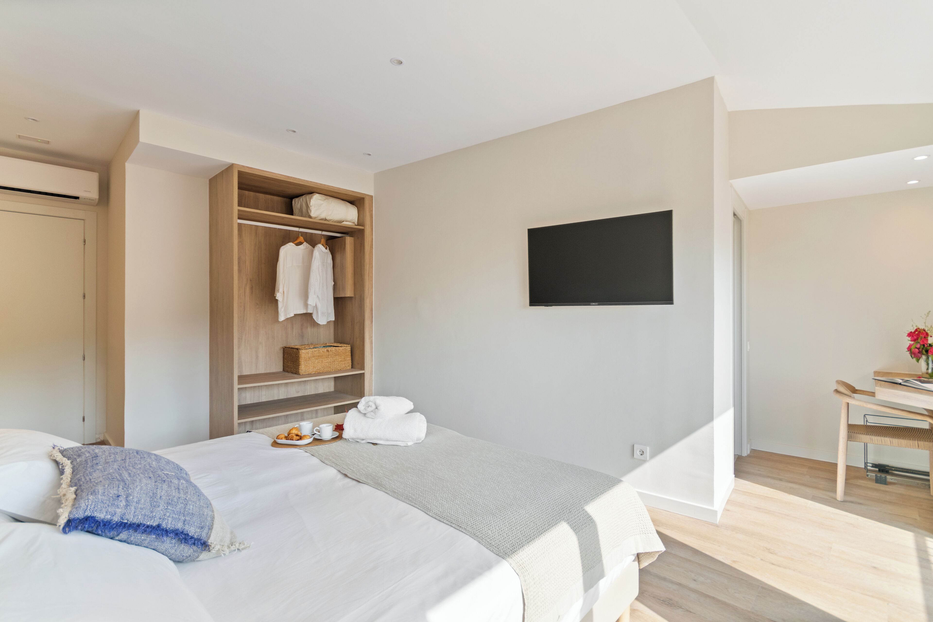 Una habitación de hotel moderna con una cama, un armario de madera, un televisor de pantalla plana y un pequeño escritorio con una silla.