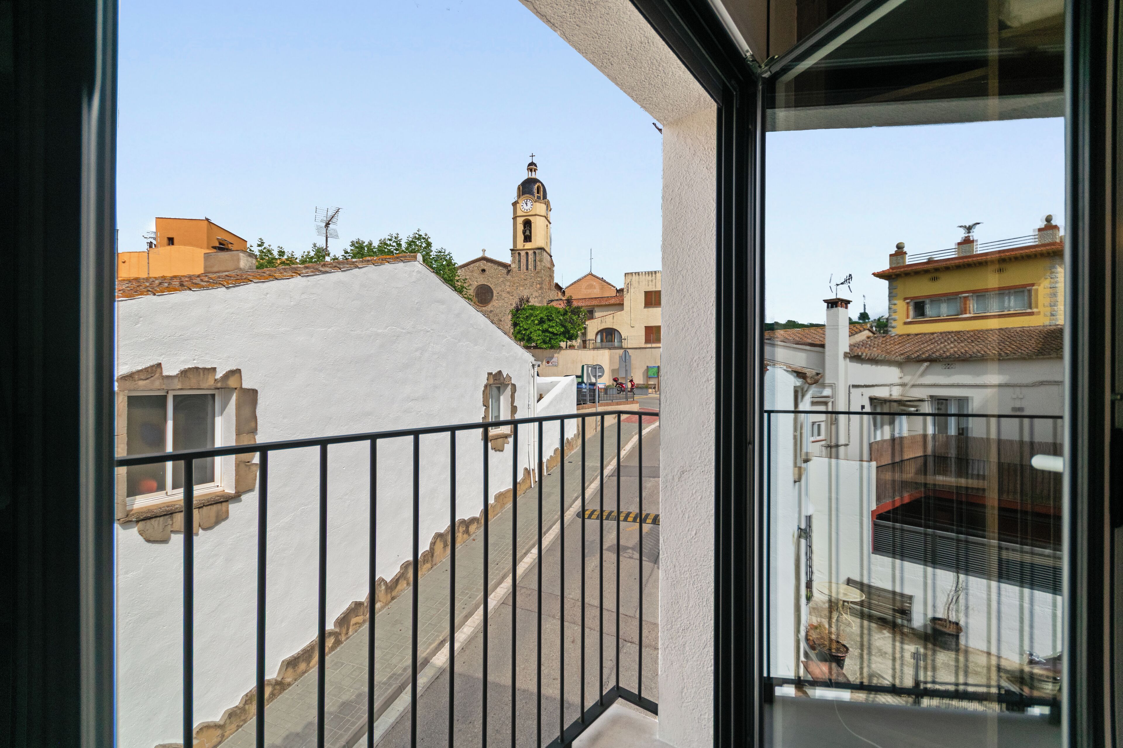 Un balcón con vista a una plaza, una torre de iglesia y edificios cercanos.