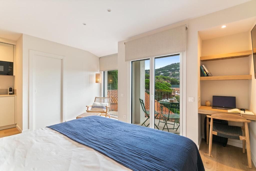 A bedroom with a bed, a desk, and a chair. There is a sliding glass door leading to an outdoor area with a table and chairs.