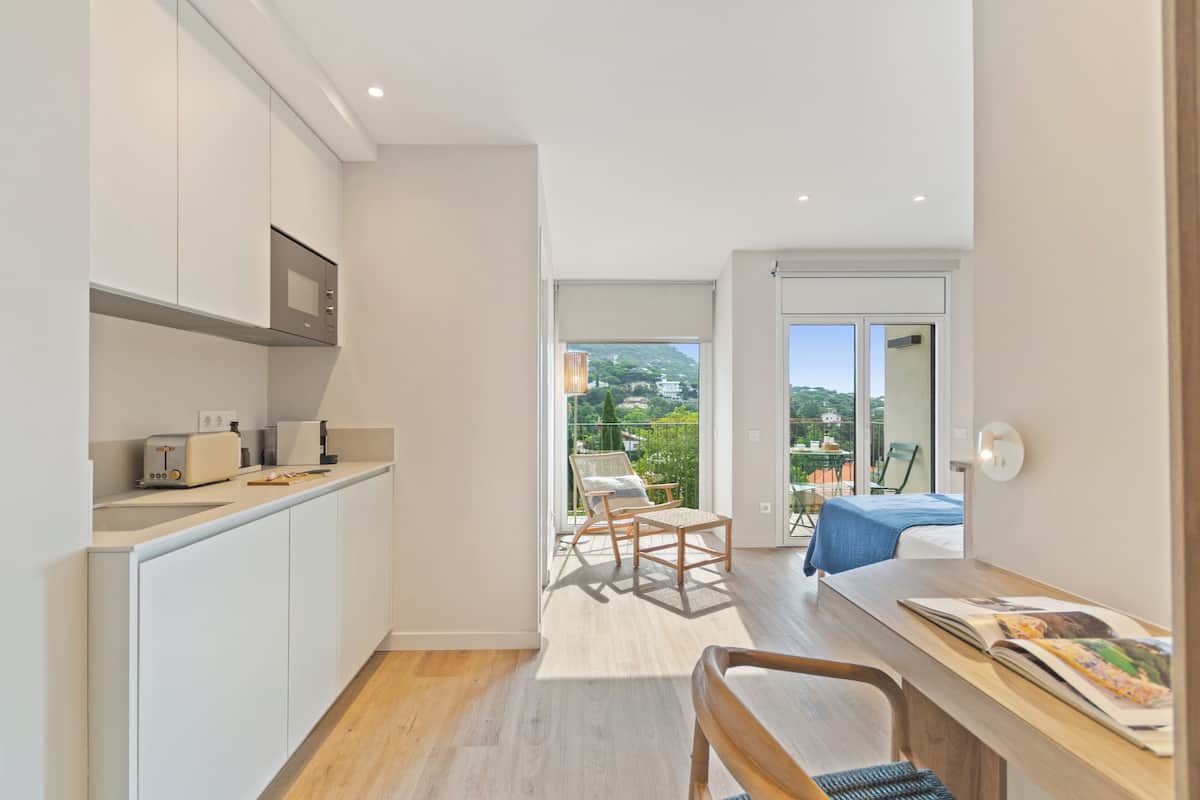 A modern kitchen with white cabinets, a wooden countertop, and a view of a balcony with outdoor furniture.