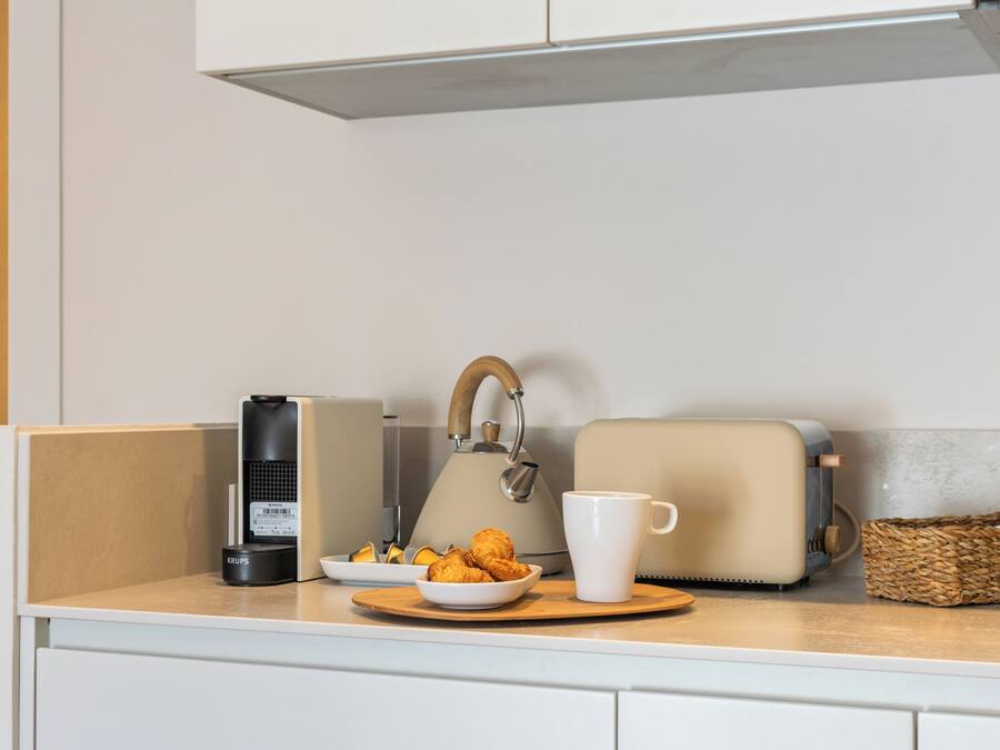A kitchen counter with a kettle, toaster, coffee maker, and a bowl of croissants.