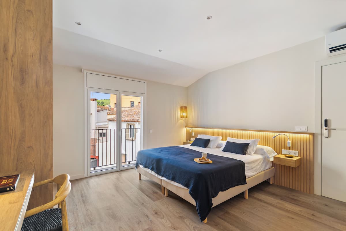 A modern bedroom with a large bed, bedside tables, a wooden desk, and a sliding glass door leading to an outdoor area.