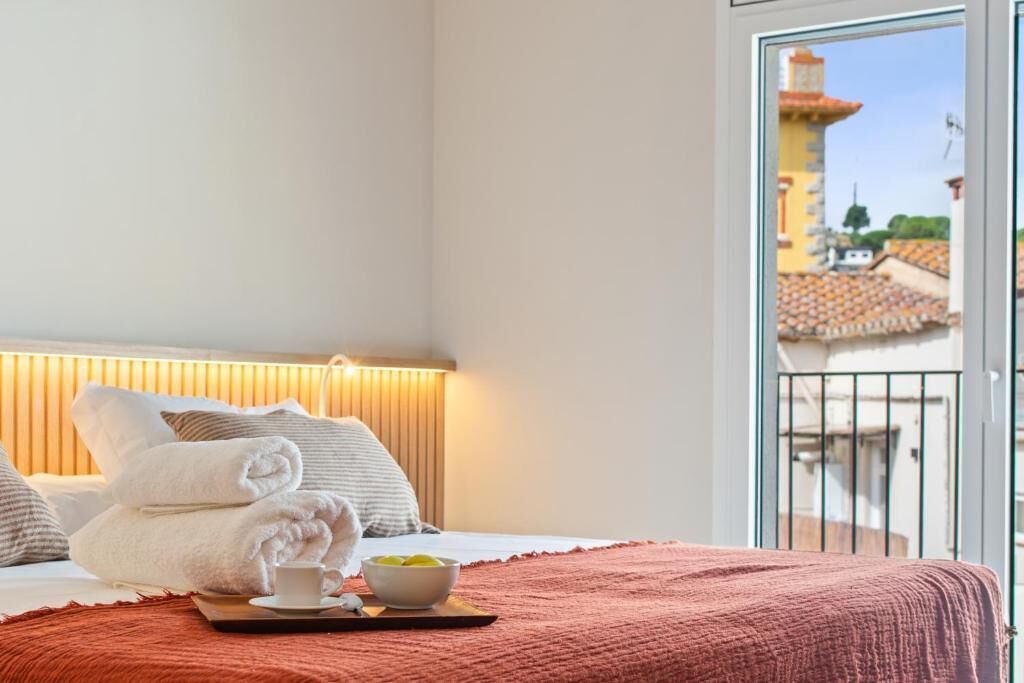 Une chambre d’hôtel avec un lit, des serviettes, un plateau avec une tasse et un bol, et un balcon donnant sur des immeubles.