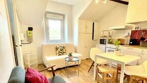 A compact living space with a sofa, a small table, a kitchen area, and a window. - Le SAINT CLEMENT in the heart of Nantes 5min from Nantes Nord train station (Nantes)
