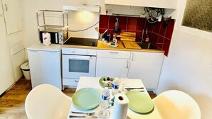 A compact kitchen with white cabinets, a small countertop, and a dining area with two white chairs and a table set for two. - Le SAINT CLEMENT in the heart of Nantes 5min from Nantes Nord train station (Nantes)