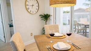 A dining area with a wooden table set for two, featuring woven placemats, wine glasses, and cutlery. A large wall clock is visible above the table. - E&A SouthWest Miami Rentals Cozy 2BD Apartment with Private Parking (miami)