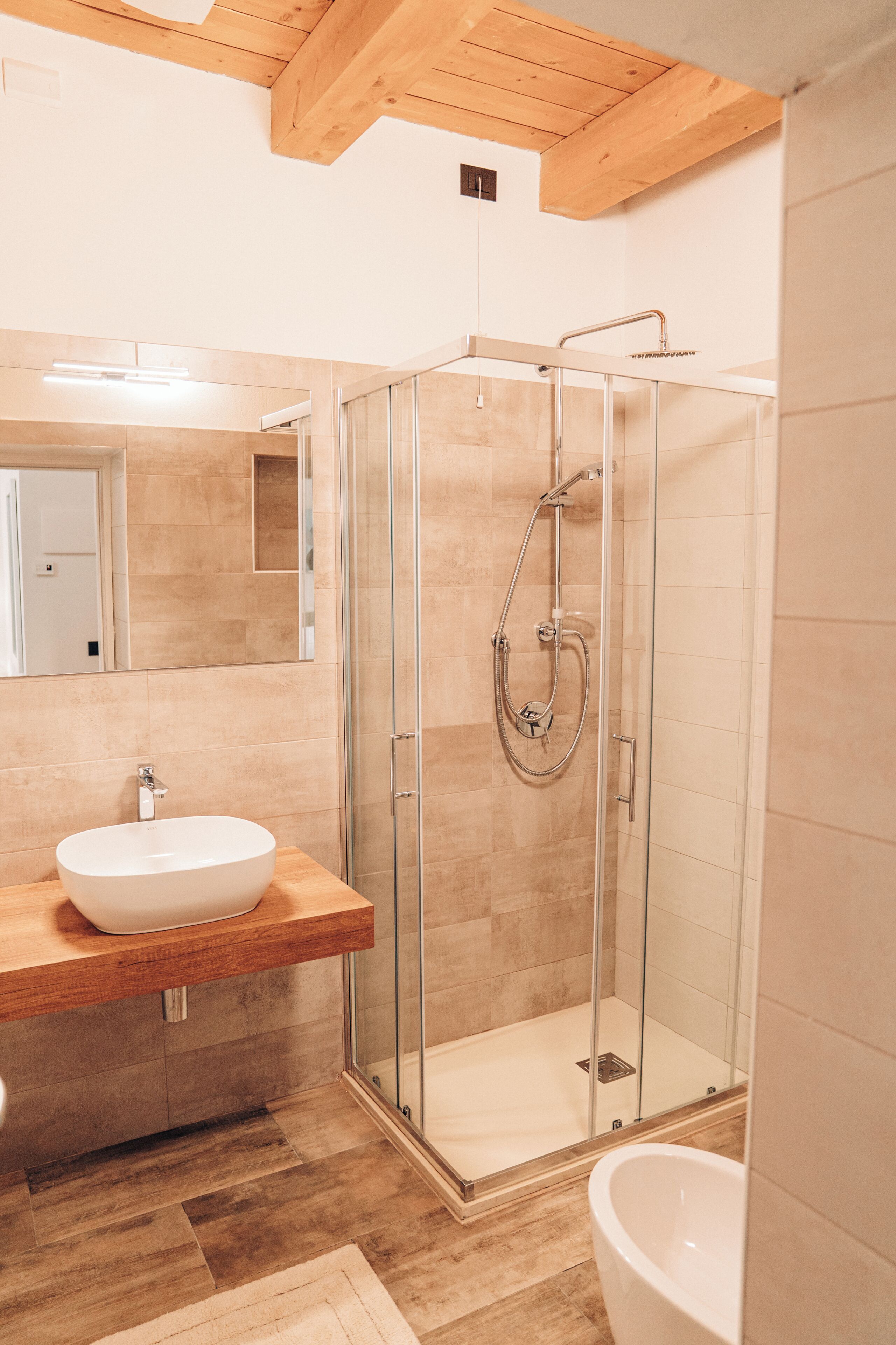 A modern bathroom with a glass-enclosed shower, a wooden vanity with a sink, and a large mirror.