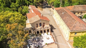 Vista aerea di un edificio con tetto in tegole rosse, un cortile con posti a sedere all'aperto e vegetazione circostante.